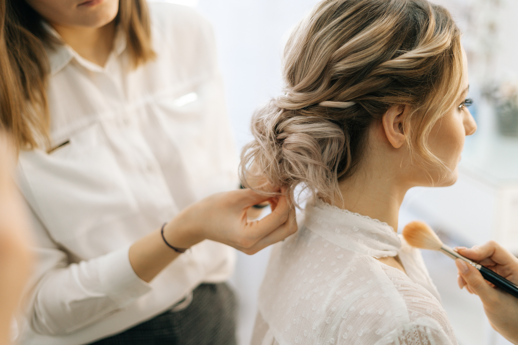 Professional female hairdresser making hairstyle wedding hairstyle for bride